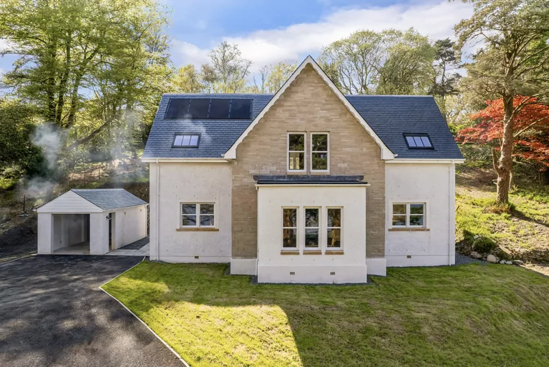Newly completed detached house with sandstone gable, slate roof and solar panels.